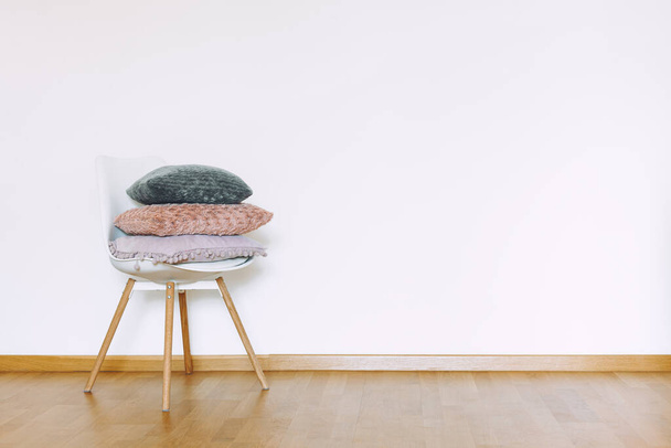 İçeride minimalist tarzda minimalist bir sandalyenin üzerinde yastıklar olan düz bir duvar modeli. Dünyevi Tarafsız Ses Arkaplanı. İçerisi, ahşap zemin ve beyaz duvarlı, havadar ışık tarzında. - Fotoğraf, Görsel