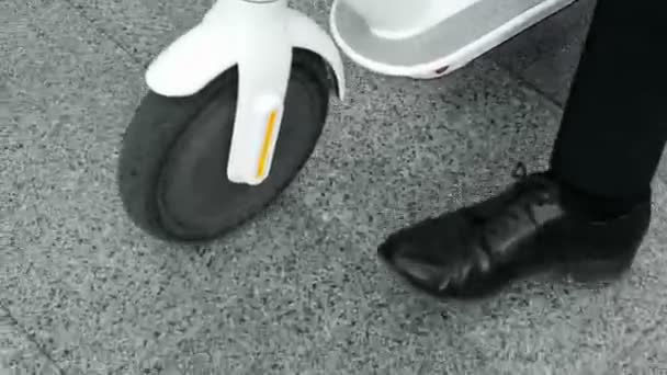 Een man in zakelijke kleding rolt een witte elektrische scooter naast zichzelf, zijaanzicht van boven - Video