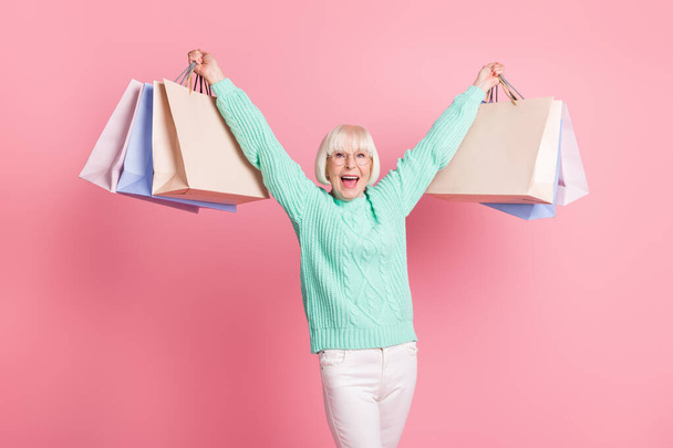Photo portrait of cheerful female pensioner showing packages after shopping wearing glasses isolated on pastel pink color background - Foto, Imagem