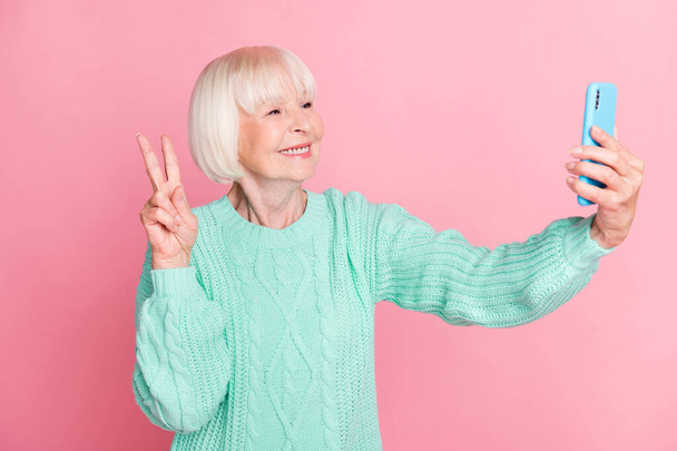 Photo portrait of grandmother taking selfie showing v-sign gesture smiling isolated on pastel pink color background - Foto, afbeelding
