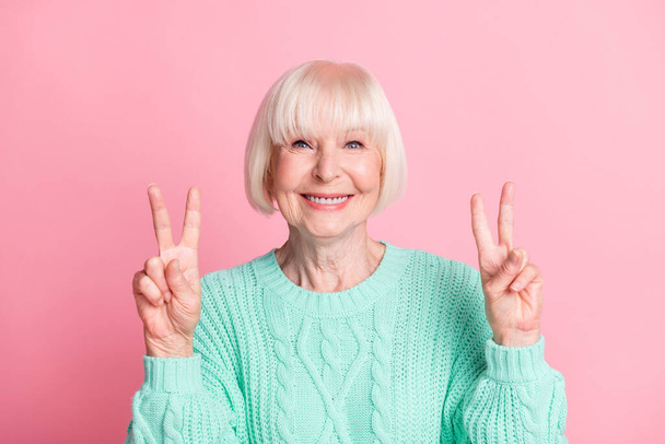 Photo portrait of cute nice senior woman in teal sweater blonde hair showing v-sign isolated on pastel pink color background - Photo, image