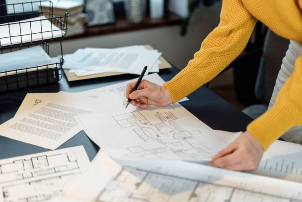 Cropped view of businesswoman working in architectural agency with blueprint, checking document, standing behind table at office, making project of building renovation - Fotoğraf, Görsel