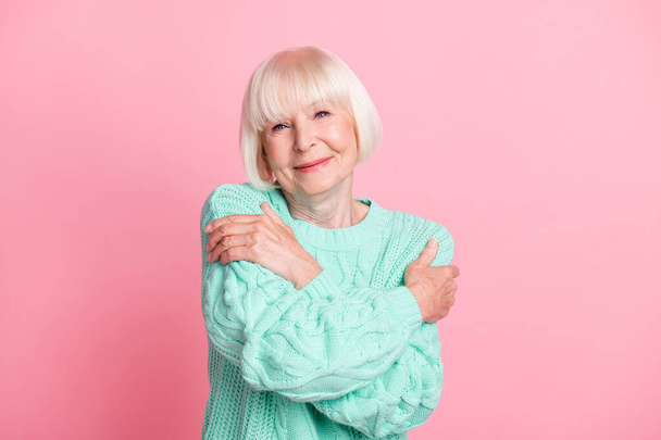 Photo portrait of cute lovely old lady with blonde hair in teal sweater embracing herself isolated on pastel pink color background - Foto, Imagen