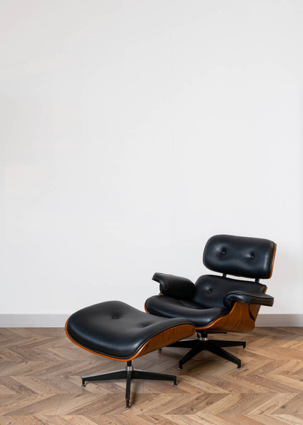 Vista vertical del sillón de cuero negro con silla cómoda para las piernas de pie en la oficina contra la pared de espacio de copia blanca en el fondo. Recreación, concepto de relajación - Foto, Imagen