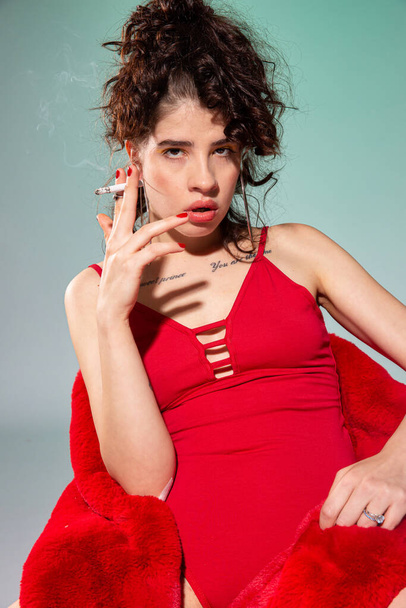 White girl model with a cigarette in red clothes isolated on green - Foto, immagini