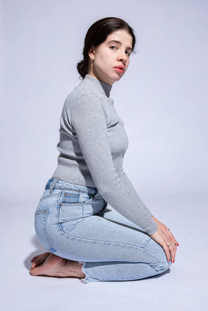Young woman sit in jeans isolated on grey - Photo, image