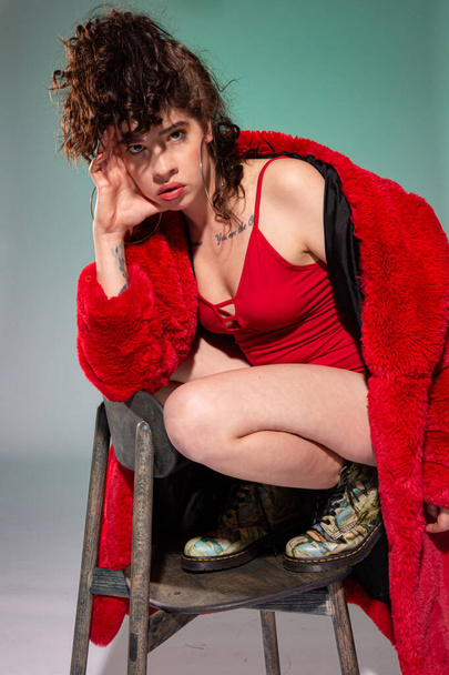 White girl model in red clothes sitting on the chair isolated on dark grey - Φωτογραφία, εικόνα