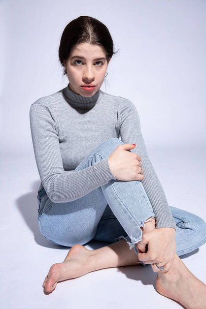 Sitting dark hair girl in roll neck isolated on grey - Photo, image