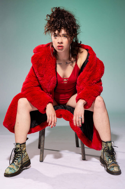 White girl model sitting on the chair in red clothes isolated on dark grey - Fotó, kép