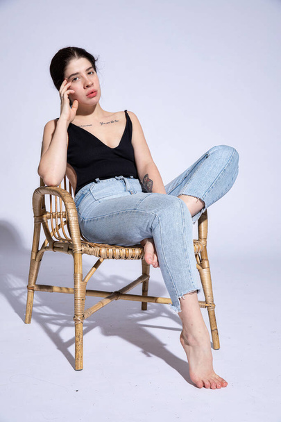 Girl in jeans sits in chair isolated on grey - Foto, afbeelding