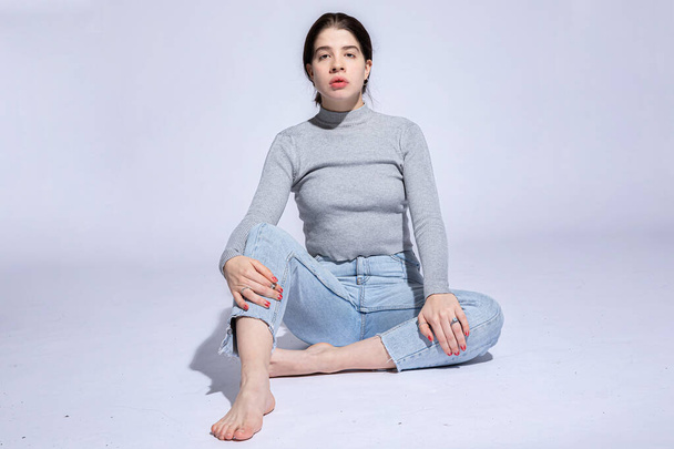 White girl sits on the floor isolated on grey - Foto, imagen