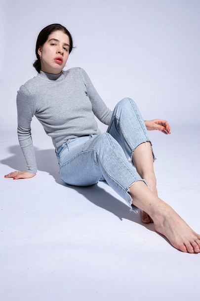 White girl in roll neck sits on the floor isolated on grey - Фото, изображение