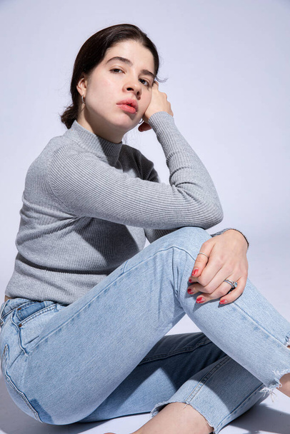 Young woman sit in jeans isolated on purple - Foto, afbeelding