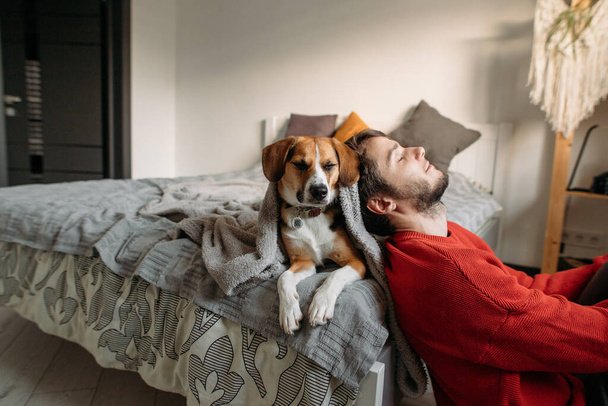 ευτυχισμένος άνθρωπος με χαριτωμένο σκυλί στην κρεβατοκάμαρα στο κρεβάτι - Φωτογραφία, εικόνα