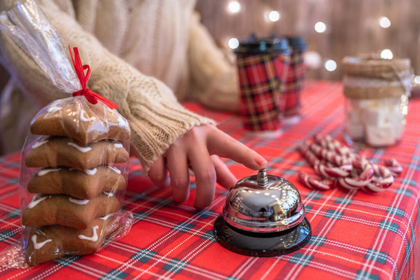 Christmas pastry shop. Woman seller, waitress ringing bell to warn that coffee in paper cup is ready. Gingerbread cookies, marshmallows in a small cozy cafe. - 写真・画像