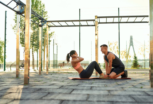 Young pair of athletes training abs on sport playground - Foto, Imagen