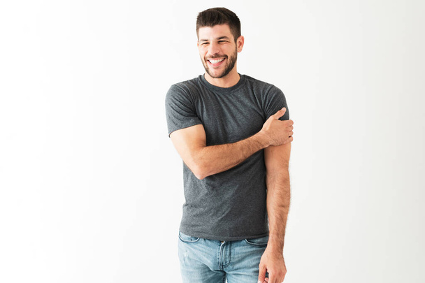 Attractive latin man in his 20s with a big smile is laughing with someone and standing in front of a white background - Photo, Image