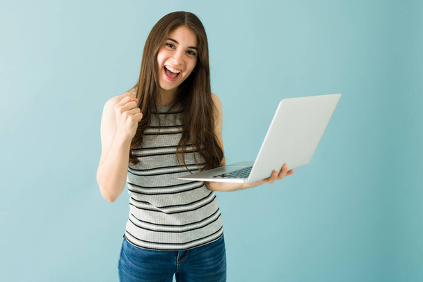 Happy caucasian young woman celebrating her success while holding a laptop. Female student finished her work on the computer - Zdjęcie, obraz