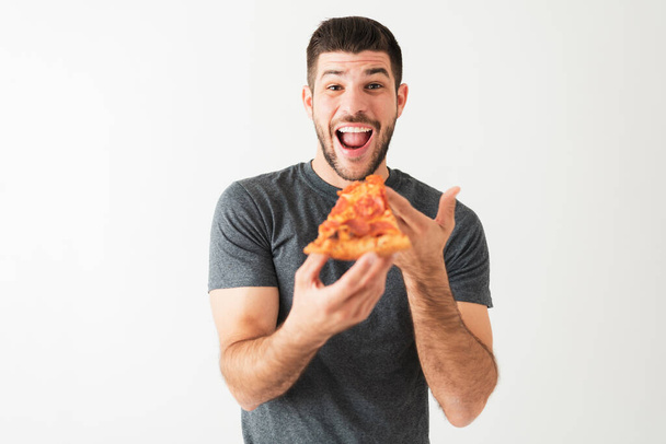 Hispanic man in his 20s is very excited and happy to eat a pepperoni pizza, white background - 写真・画像