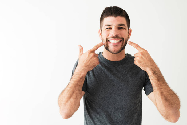 Latin man pointing to his big and bright smile. Portrait of a handsome man with white teeth is smiling and looking very happy  - Photo, Image