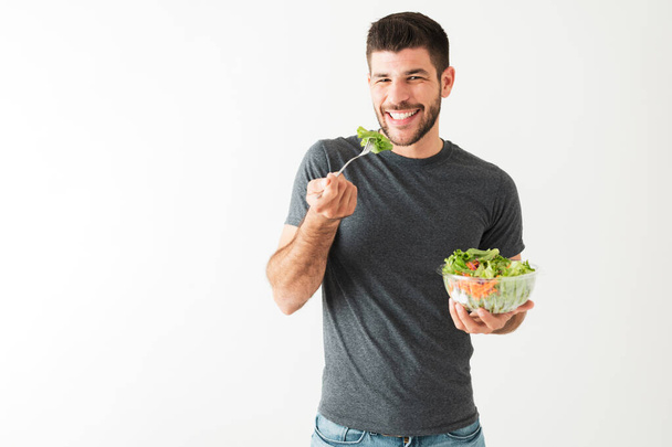 Muotokuva houkutteleva ja kunto mies hänen 20s syö vihanneksia haarukalla ja tilalla vihreä salaatti  - Valokuva, kuva