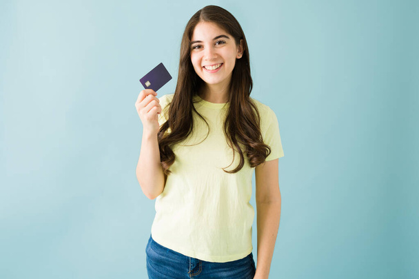 Mujer joven caucásica bien parecido está usando ropa casual y sonriendo mientras sostiene una tarjeta de crédito sobre un fondo azul - Foto, imagen