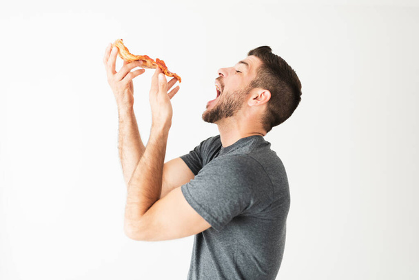 Side view of a hispanic man in his 20s with a craving of pepperoni pizza against a white background - Fotografie, Obrázek