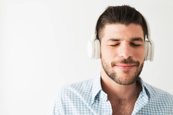 Zbliżenie atrakcyjnego mężczyzny słuchającego muzyki ze słuchawkami. Młody człowiek cieszący się piosenką z zamkniętymi oczami  - Zdjęcie, obraz