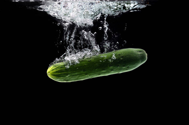 Green bio cucumber sinking under water against black background - Foto, afbeelding