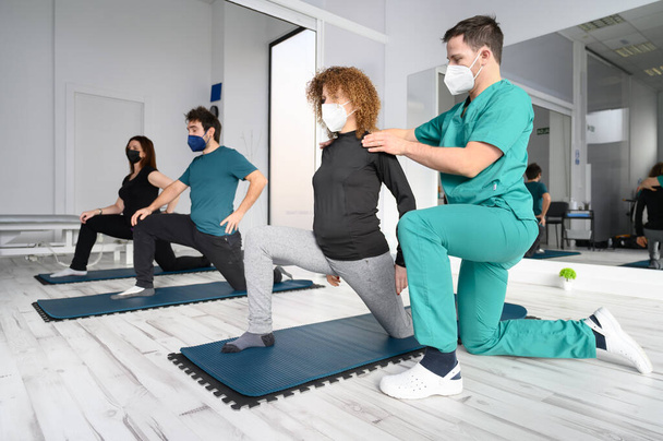 Группа лиц на ковриках для йоги при содействии физиотерапевта в реабилитационной клинике. - Фото, изображение
