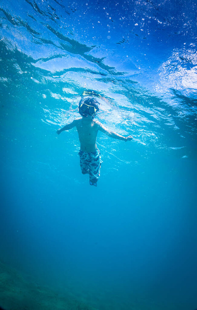 Búvármaszkos fiú úszik a víz alatt. - Fotó, kép