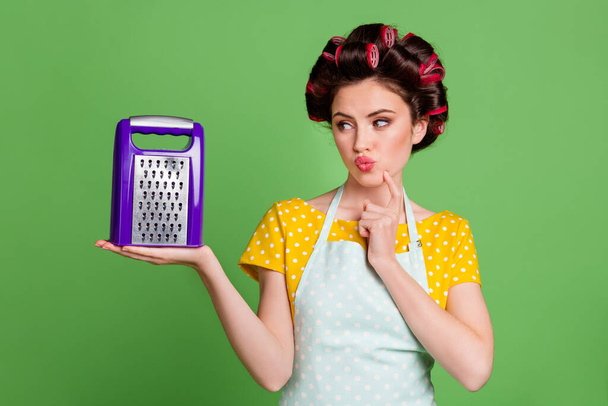 Portrait of her she nice-looking attractive pretty glamorous curious minded maid wearing curlers holding on palm grater thinking creating recipe solution pout lips isolated over green color background - Valokuva, kuva