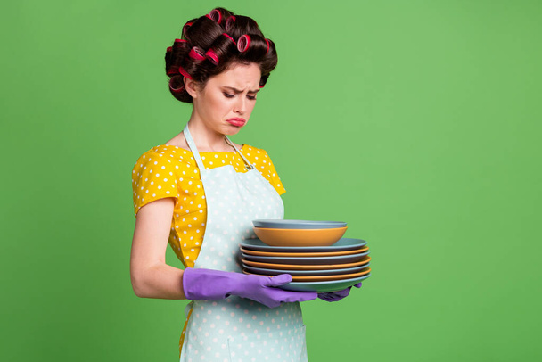Portrait of her she nice attractive glamorous tired depressed maid wearing curlers holding in hands pile stack plates everyday routine isolated over green color background - Фото, изображение