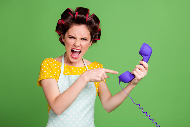Portrait of her she nice attractive fashionable glamorous evil mad fury wife wearing curlers holding in hands showing headset yelling bad mood isolated over green color background - Foto, afbeelding
