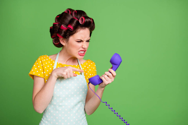 Stop scam me. Furious crazy retro girl call ring telephone have friend quarrel offense scream point finger cord wear yellow dotted dress skirt hair rollers isolated green color background - 写真・画像