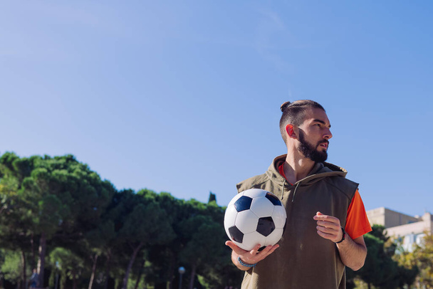 portrait of an attractive hipster football player with the ball in his hand, concept of healthy lifestyle and urban sport in the city, copy space for text - 写真・画像