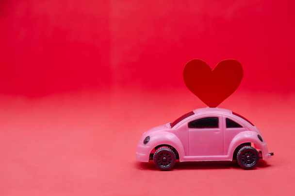 Small pink car with a red heart on the roof of the car with copy space. Festive bright background - Photo, Image