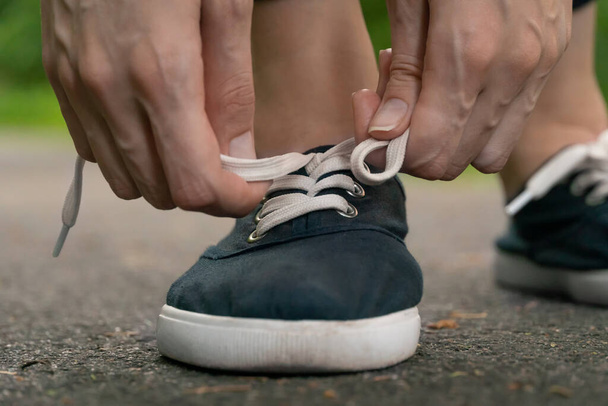 Lähikuva naisten käsissä sitominen kengännauhat tummansininen lenkkarit lenkillä metsässä. - Valokuva, kuva
