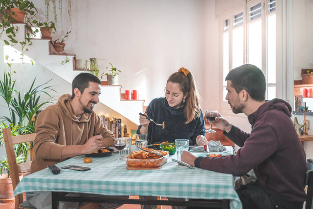Friends having fun during dinner at dining table. Cheerful young people eating, toasting and enjoying with friends at home. - Fotoğraf, Görsel