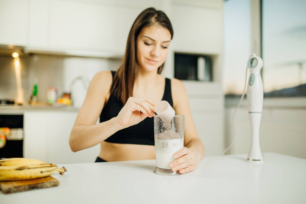 Woman with immersion blender making banana chocolate protein powder milkshake smoothie.Adding a scoop of low carb whey protein mix to shake after a home workout.Diet after the gym.Healthy lifestyle - 写真・画像