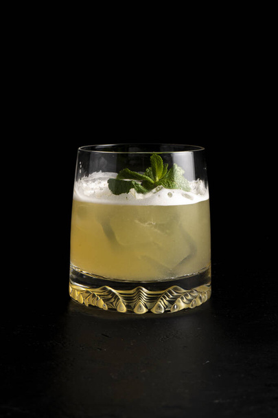 Whiskey sour cocktail. Cold alcoholic cocktail of quail egg protein, lemon juice, sugar syrup, bourbon, bitter, mint and ice in a transparent glass on a black background. - Foto, immagini