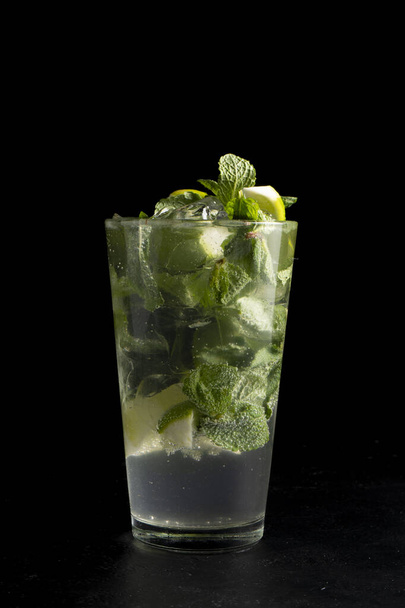Mojito cocktail. Cold alcoholic cocktail of lime, mint, sugar syrup, white rum, soda and ice in a transparent glass on a black background. - Фото, изображение