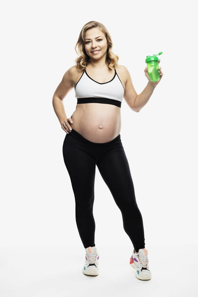 Young smiling pregnant blonde woman in sportswear stands. Healthy motherhood. Full height. Isolated on white background. Vertical. - Φωτογραφία, εικόνα