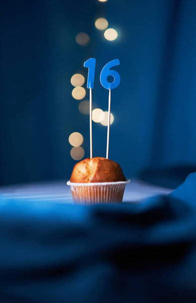 Bolo de aniversário ou muffin com número dezesseis (16) e luzes no fundo azul. Conceito de aniversário ou aniversário - Foto, Imagem