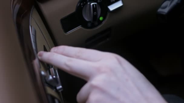 lähikuva miespuolisesta kädestä painamalla säätöpainikkeita sähköistuimen säätämiseksi auton sisällä. Sisäoven istuimen säätöpainikkeen kytkin. 4K-video - Materiaali, video