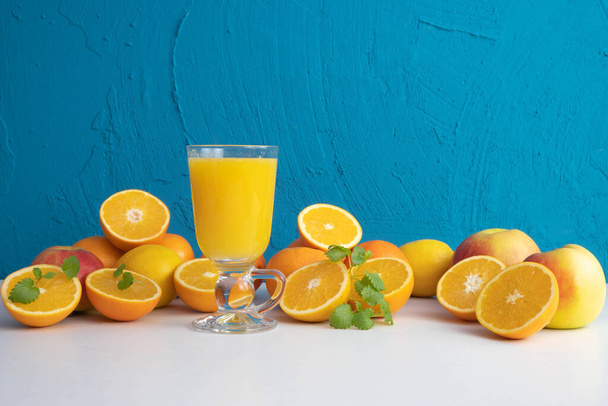 friss narancslé egy pohárban és az asztalon sok friss narancs és gyümölcs, kék alapon - Fotó, kép