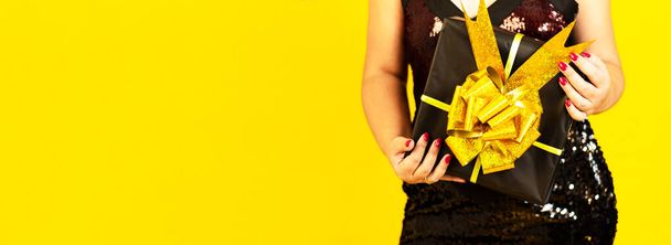 Wide banner. Female hands in dress holding gift box over copy space yellow color background, celebration sale concept womens day and gifts. - Fotografie, Obrázek