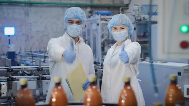 Arbeiter in Masken und Uniform zeigen nahe Förderband Daumen hoch - Filmmaterial, Video
