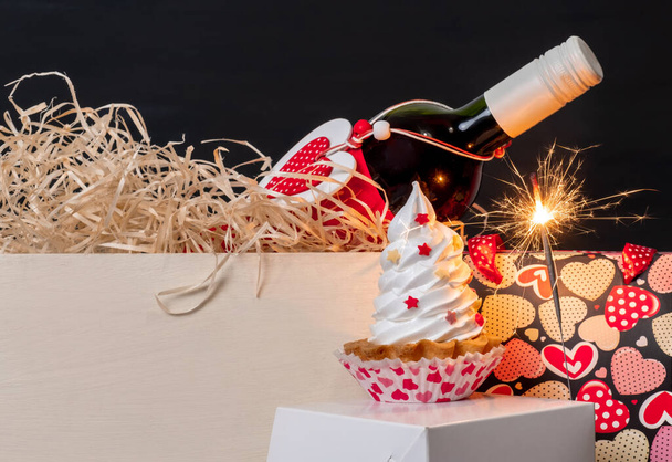 Спарклер, бутылка вина, сумка с сердечками и безе торт на черном фоне на День Святого Валентина. - Фото, изображение