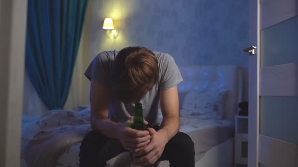 Πορτρέτο ενός μοναχικού άνδρα με κατάθλιψη κάθεται σε ένα κρεβάτι με ένα μπουκάλι αλκοόλ - Πλάνα, βίντεο